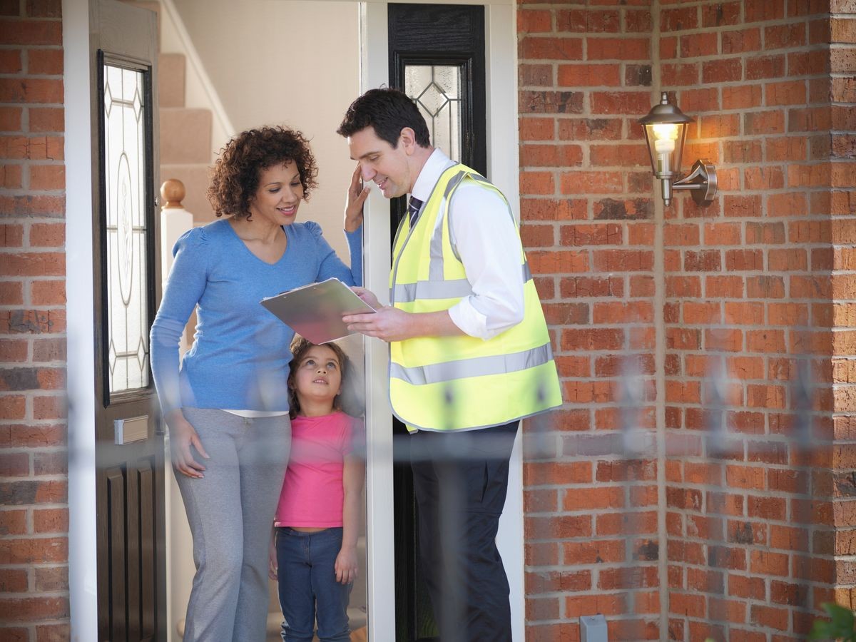 Woman and daughter talking to energy advisor at front door of house